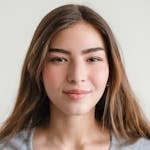 Close-up headshot of a smiling young woman with long hair wearing a casual top indoors.