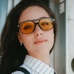 Close-up portrait of a young woman wearing yellow sunglasses and a striped shirt. Modern and bold style.