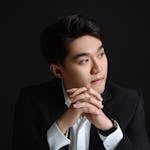 Studio portrait of a confident businessman in a black suit with hands clasped thoughtfully.